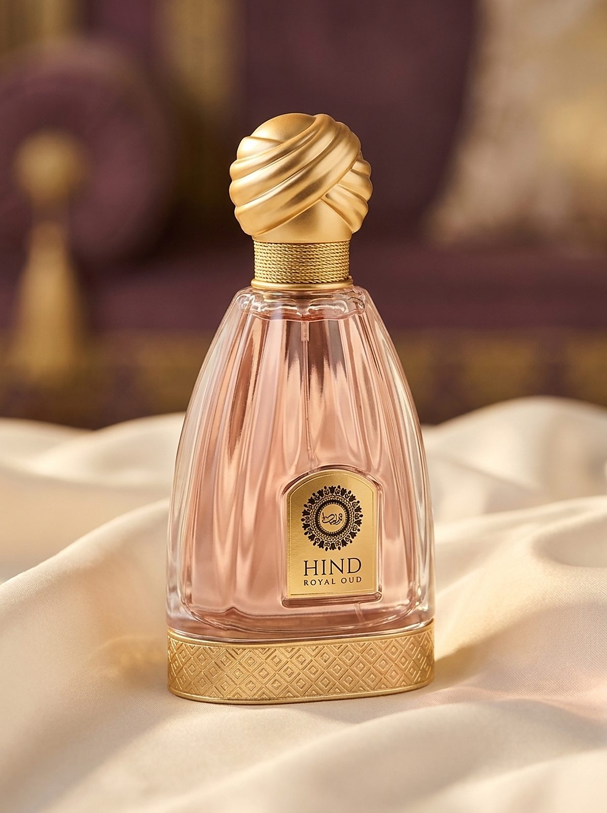Hind Royal Oud blush eau de parfum in fluted pink glass with a brushed-gold turban cap, resting on ivory silk